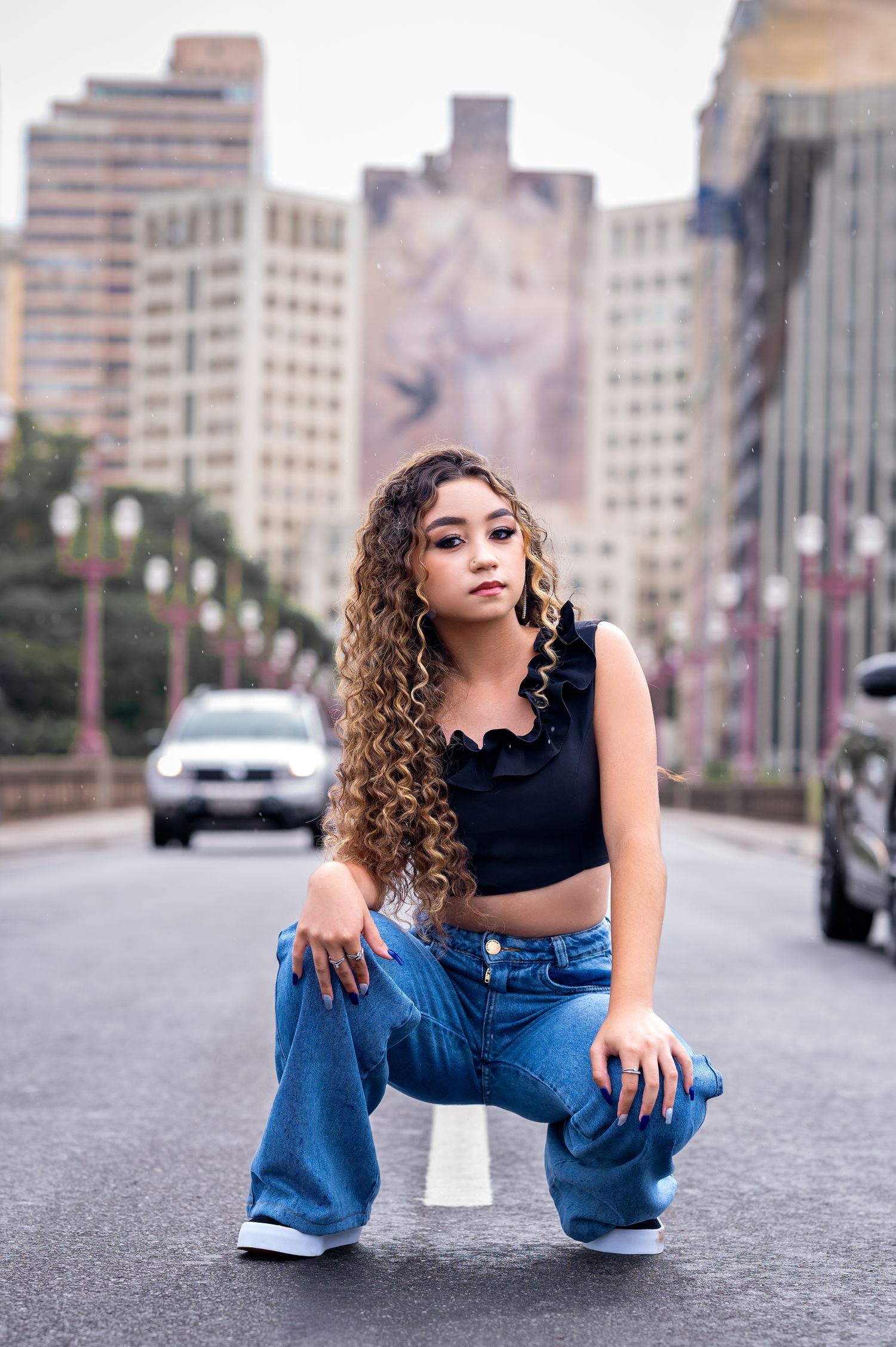 Confident young woman with curly hair posing on a city street with buildings in the background.