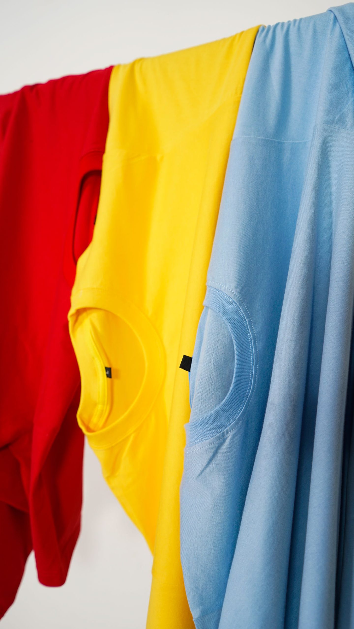 Vivid primary colored T-shirts hanging to dry on a line, showcasing red, yellow, and blue fabrics.